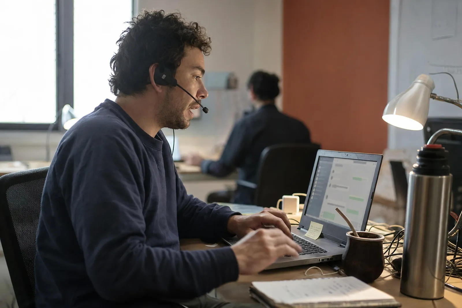 Operador con auricular respondiendo consultas de clientes en una laptop en una oficina chica