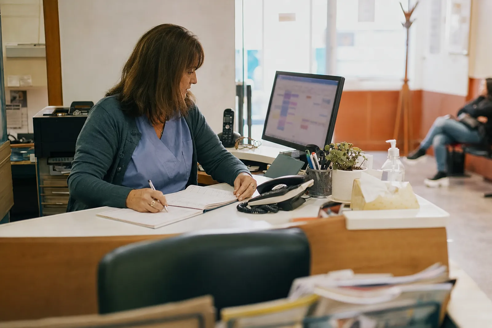 Recepcionista de un consultorio anotando turnos en una agenda frente al monitor