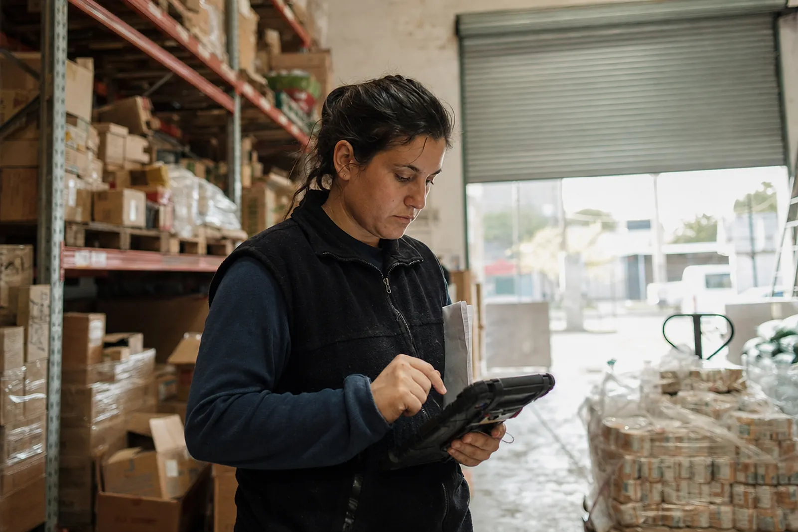 Empleada de un depósito revisando pedidos en una tablet entre estanterías
