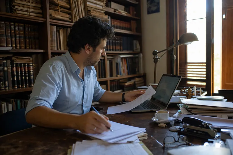 Young lawyer reviewing printed documents and a laptop in an office lined with bookshelves